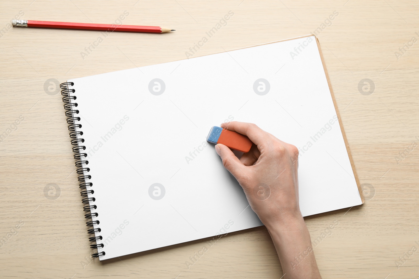 Photo of Woman erasing something in notebook at wooden table, closeup