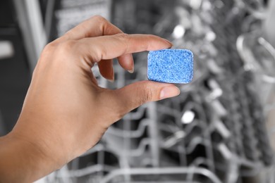 Photo of Woman putting detergent tablet into open dishwasher in kitchen, closeup