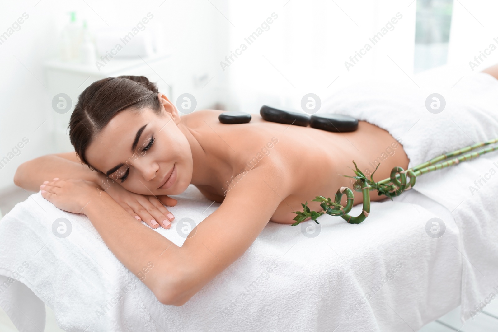 Photo of Beautiful young woman getting hot stone massage in spa salon