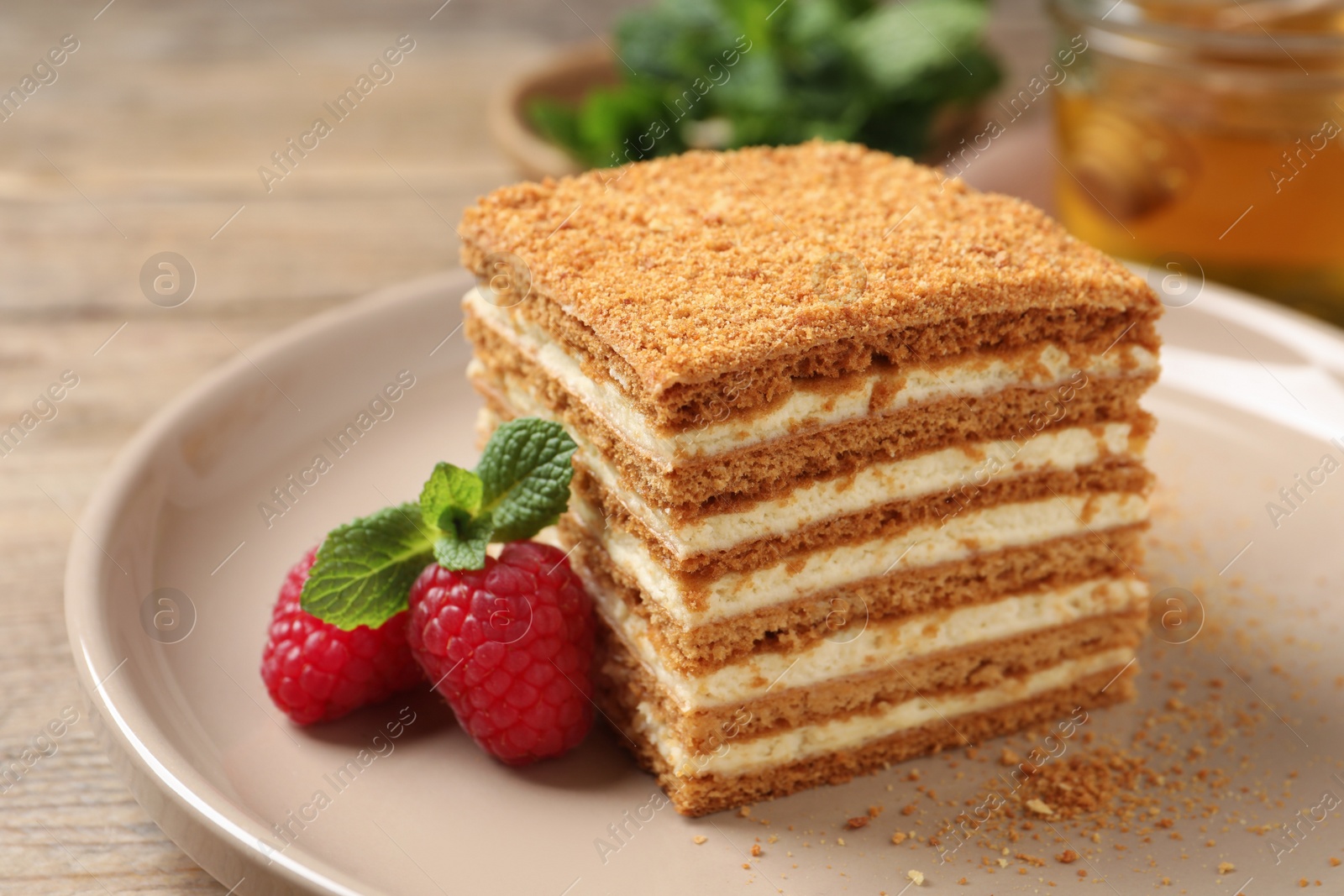 Photo of Slice of delicious layered honey cake served with mint and raspberries on plate, closeup