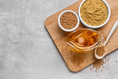 Photo of Jug of natural oil, mustard seeds and powder on grey table, top view. Space for text