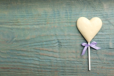 Photo of Chocolate heart shaped lollipop on light blue wooden table, top view. Space for text