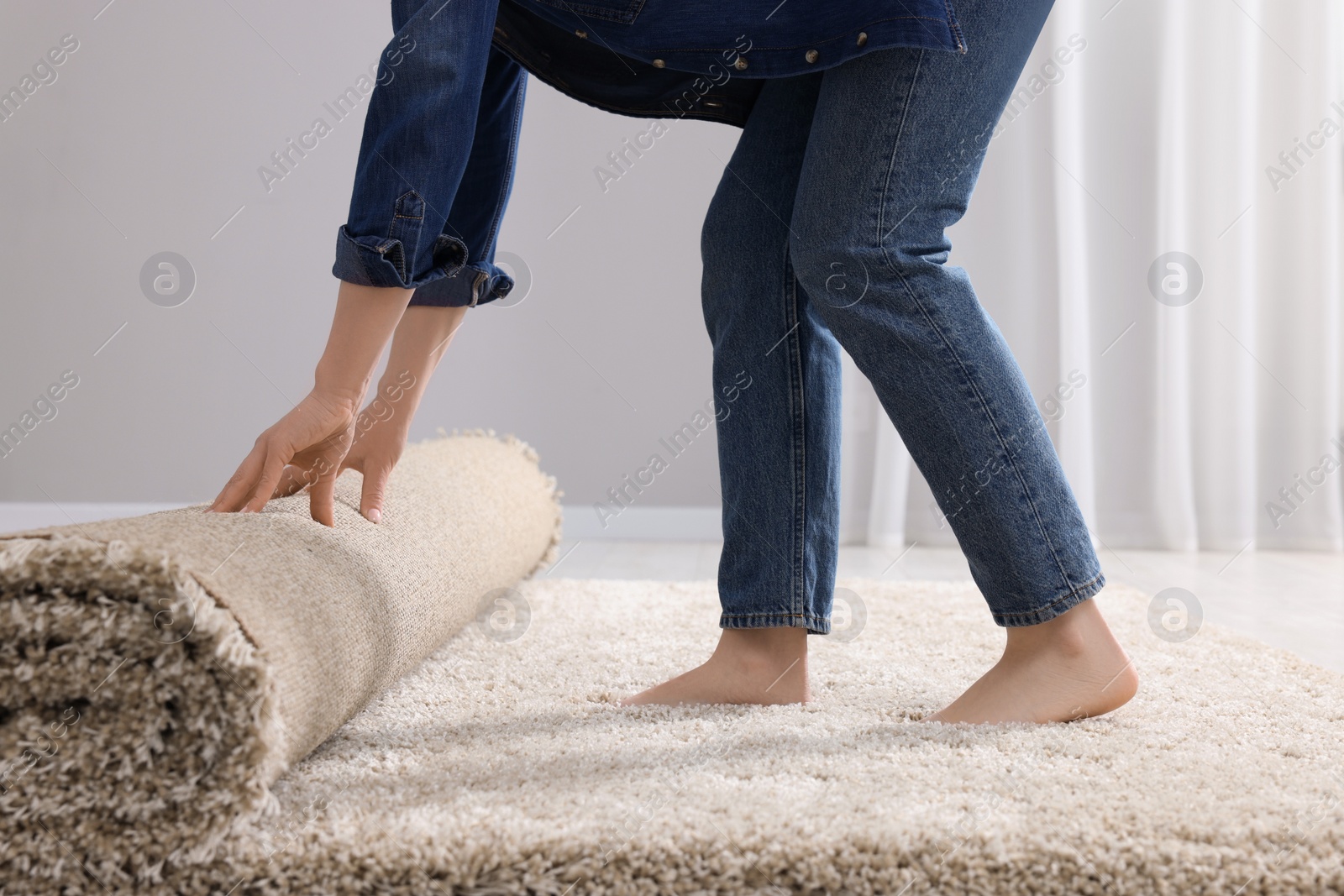 Photo of Woman unrolling carpet on floor in room, closeup