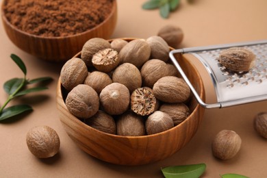 Photo of Nutmeg powder, seeds, grater and green leaves on light brown background, closeup