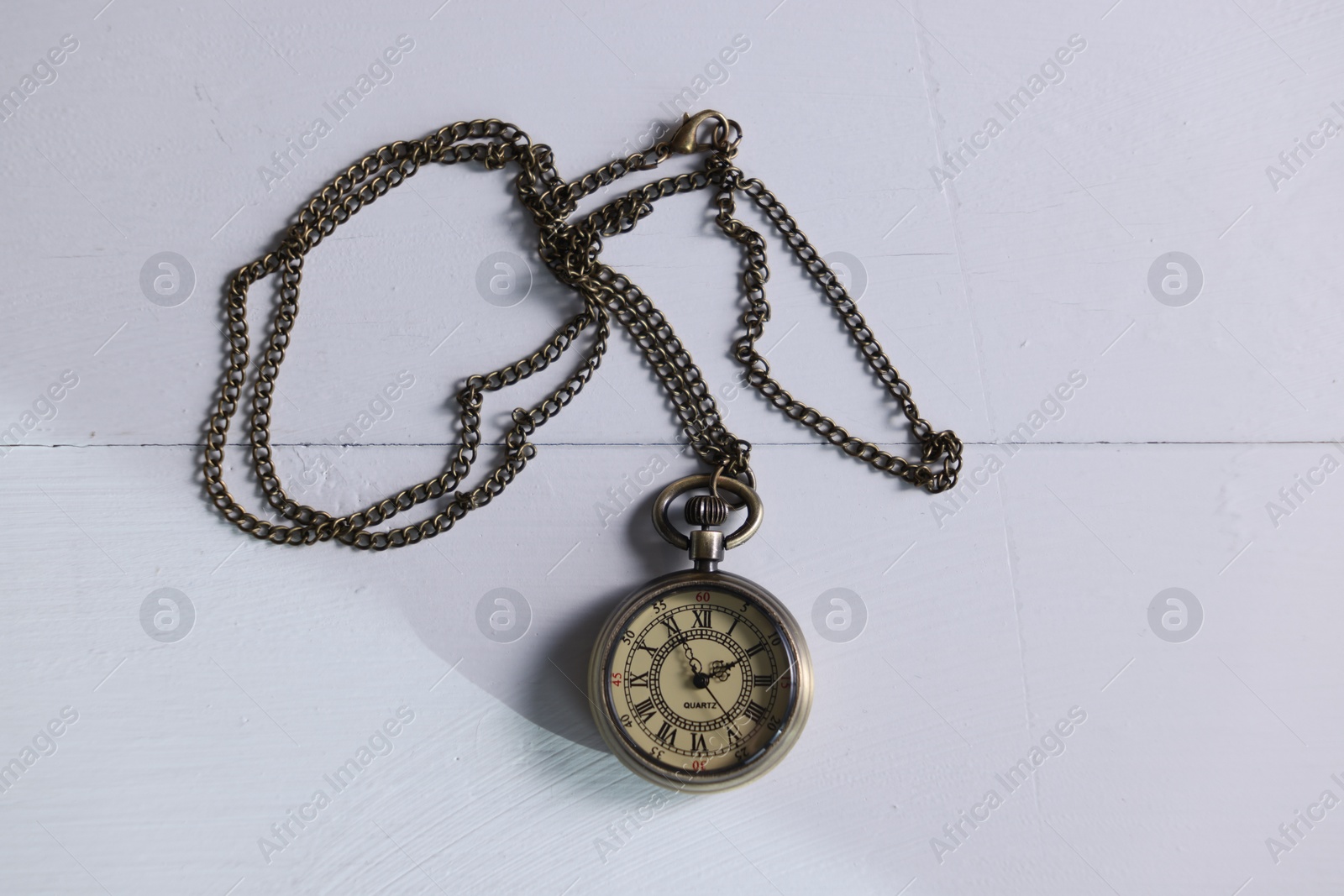 Photo of Pocket clock with chain on white wooden table, top view