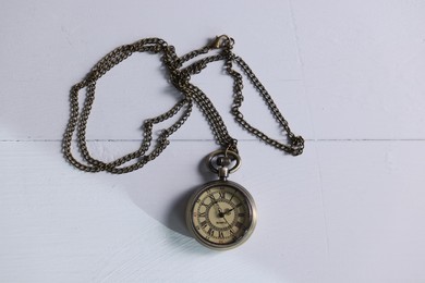 Pocket clock with chain on white wooden table, top view