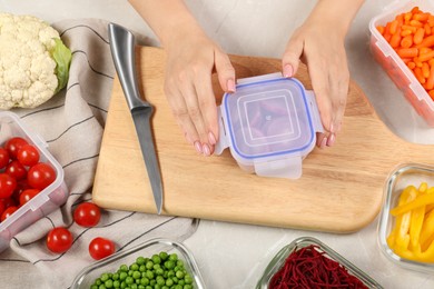 Woman closing container with lid at light gray table, top view. Food storage