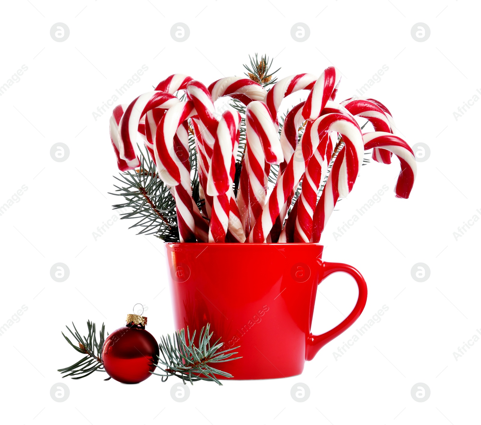 Image of Many sweet candy canes in red cup with fir tree branches near bauble on white background. Christmas treat