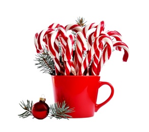 Many sweet candy canes in red cup with fir tree branches near bauble on white background. Christmas treat