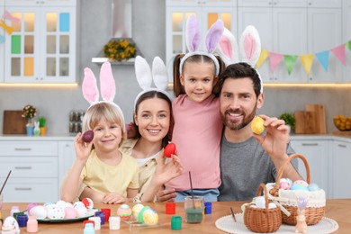 Photo of Happy family painting Easter eggs at table in kitchen
