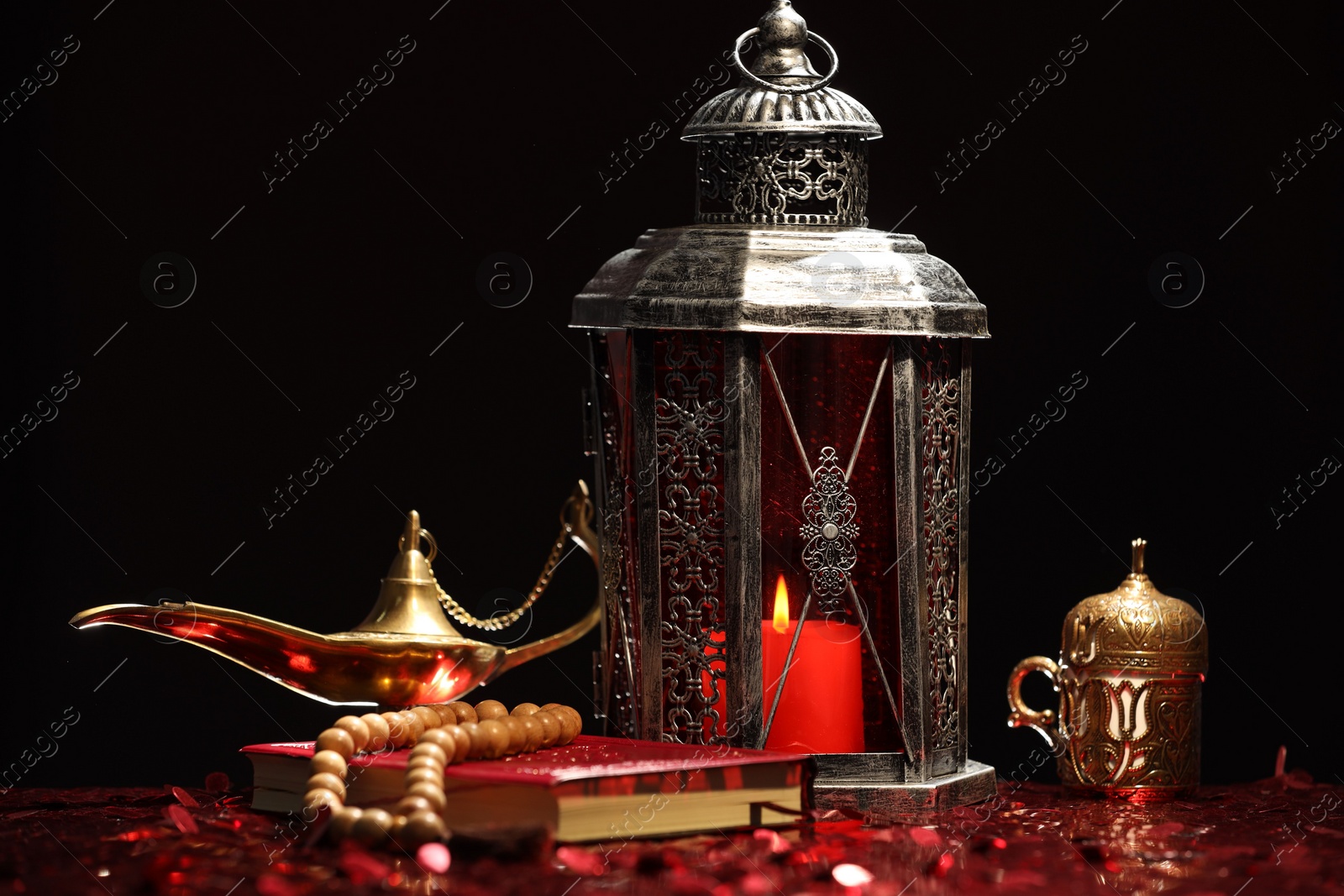 Photo of Arabic lantern, Quran, misbaha and Aladdin magic lamp on shiny red table