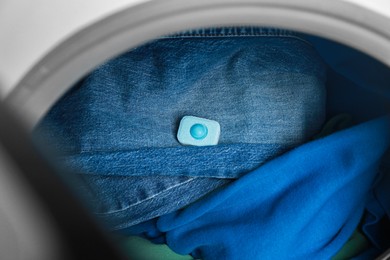 Photo of Water softener tablet on clothes in washing machine, closeup