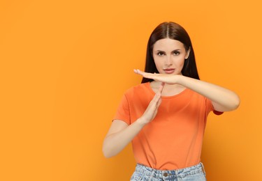 Photo of Woman showing time out gesture on orange background. Space for text
