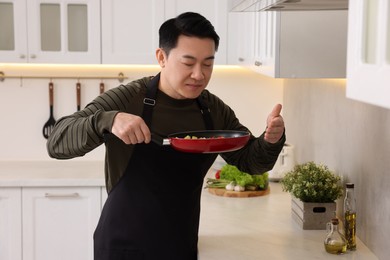Man with frying pan smelling dish after cooking in kitchen