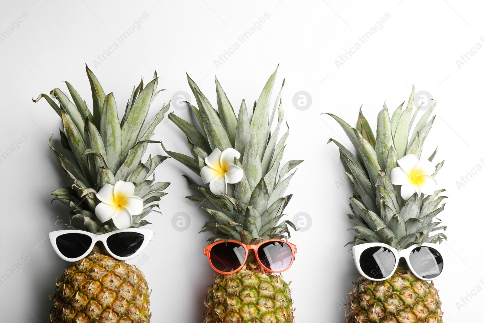 Photo of Pineapples with sunglasses and plumeria flowers on white background, top view. Creative concept