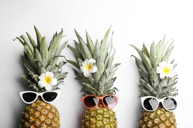 Photo of Pineapples with sunglasses and plumeria flowers on white background, top view. Creative concept