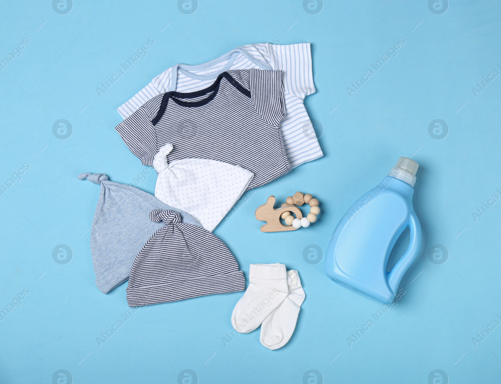 Photo of Flat lay composition with bottle of detergent and children's clothes on light blue background