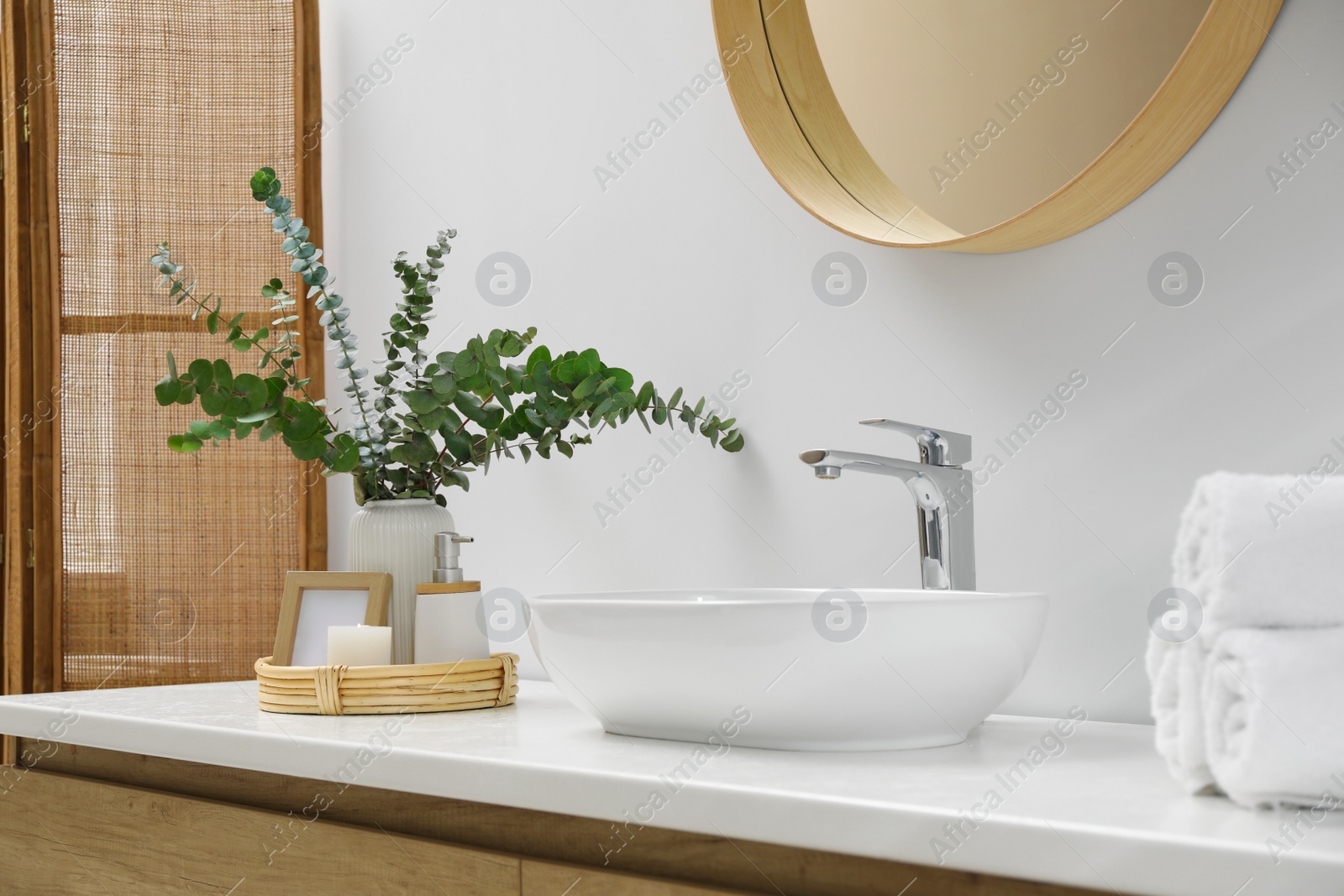 Photo of Vase with eucalyptus branches and toiletries near vessel sink in bathroom. Interior design