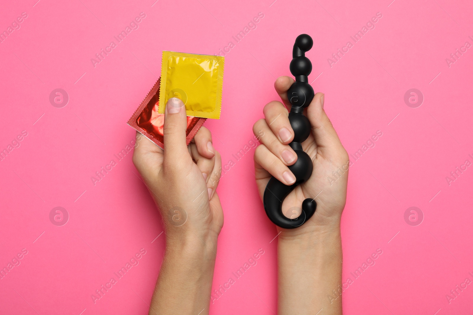 Photo of Woman with anal balls beads and condoms on pink background, top view. Sex game