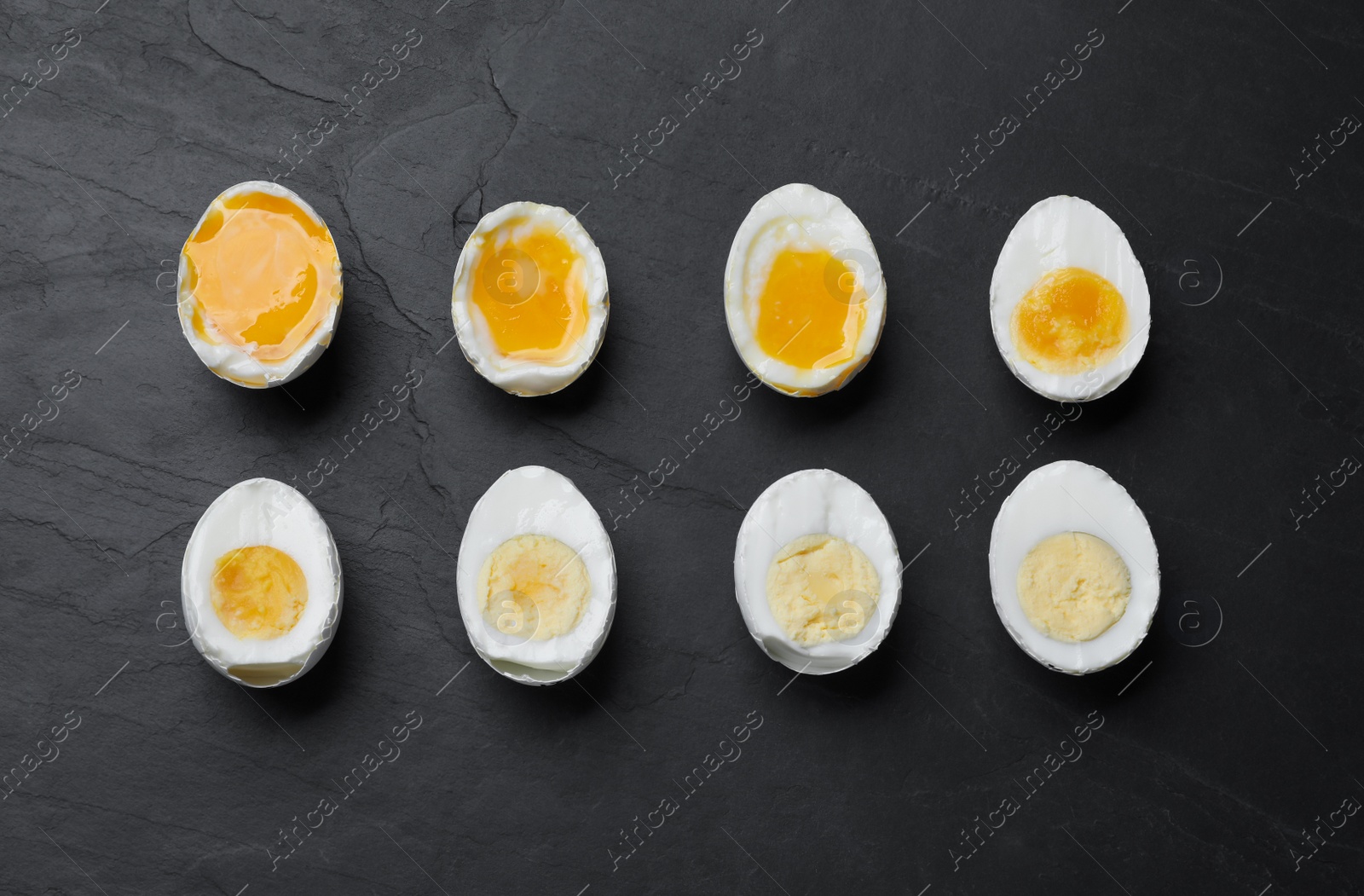 Photo of Different readiness stages of boiled chicken eggs on black table, flat lay