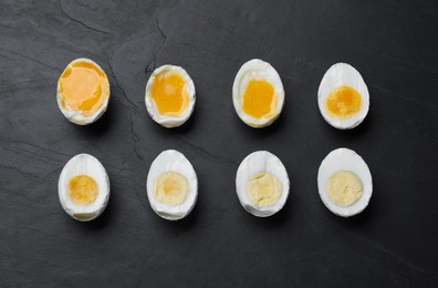 Photo of Different readiness stages of boiled chicken eggs on black table, flat lay