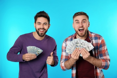 Happy young men with money on color background