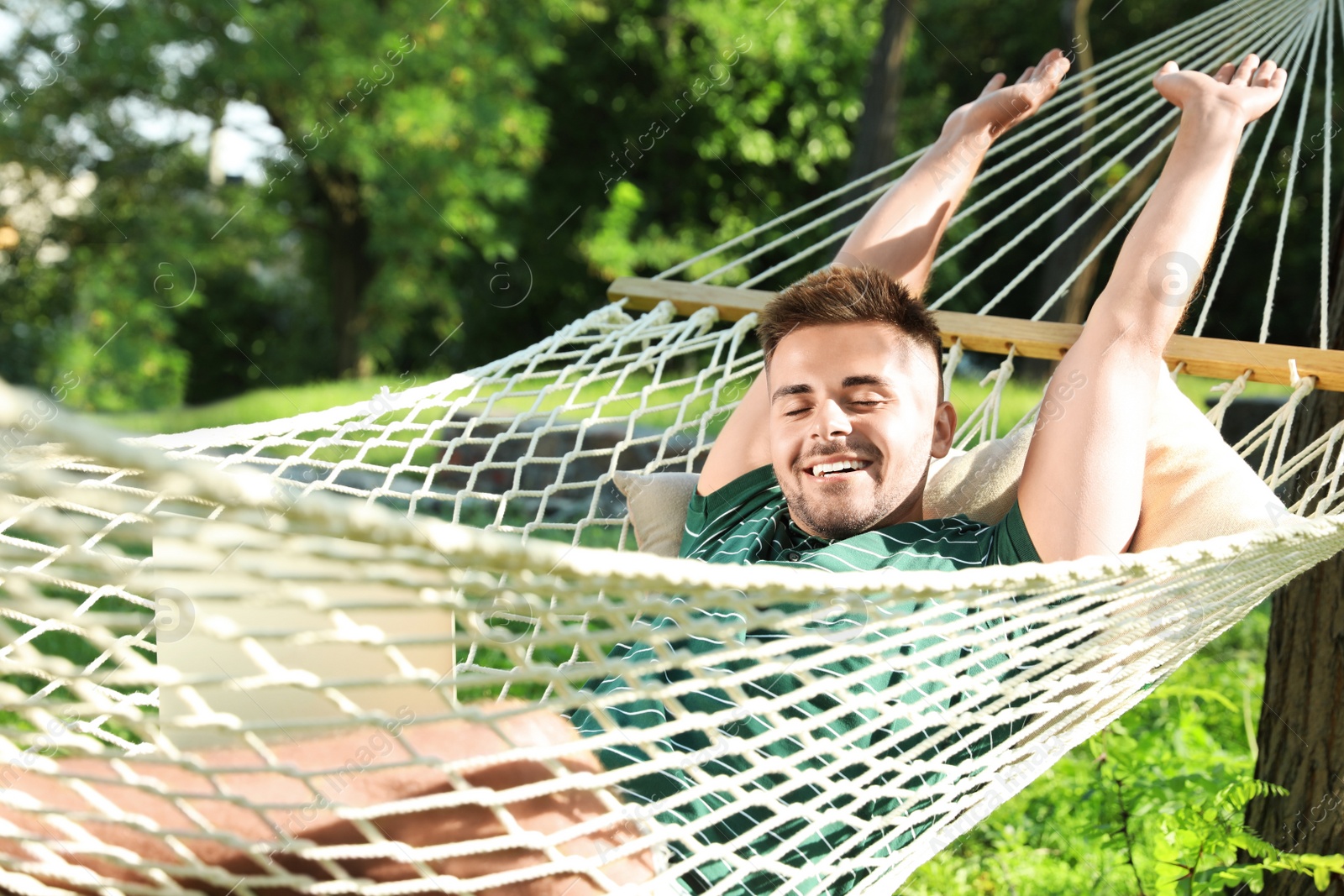 Photo of Young man with laptop resting in comfortable hammock at green garden