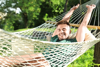 Young man with laptop resting in comfortable hammock at green garden