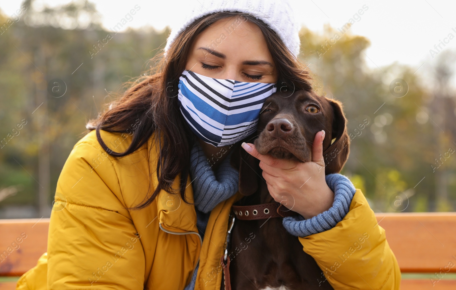 Photo of Woman in protective mask with German Shorthaired Pointer outdoors. Walking dog during COVID-19 pandemic