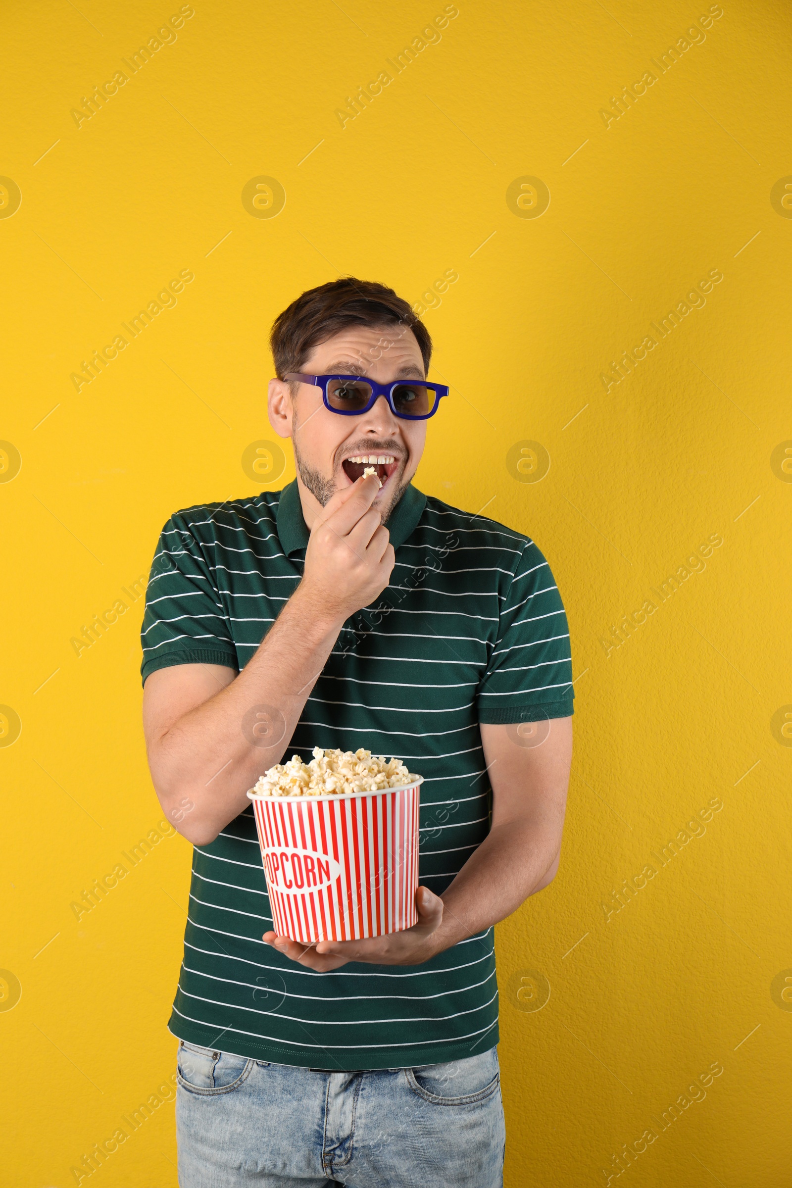 Photo of Man with 3D glasses eating tasty popcorn on color background