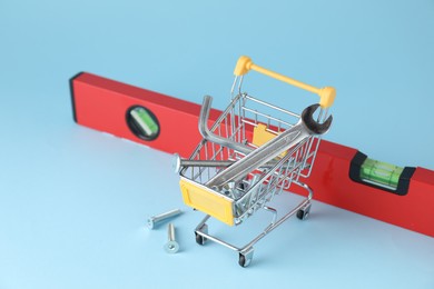 Photo of Shopping cart with different construction tools on light blue background