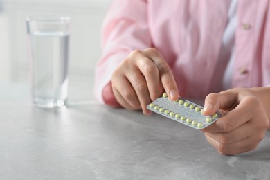 Photo of Woman taking oral contraception pill at light grey marble table indoors, closeup