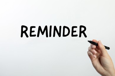 Woman writing word REMINDER on glass against white background, closeup