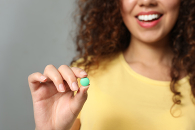 Photo of African-American woman with vitamin pill on light grey background, closeup