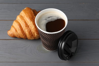 Coffee to go. Paper cup with tasty drink and croissant on grey wooden table