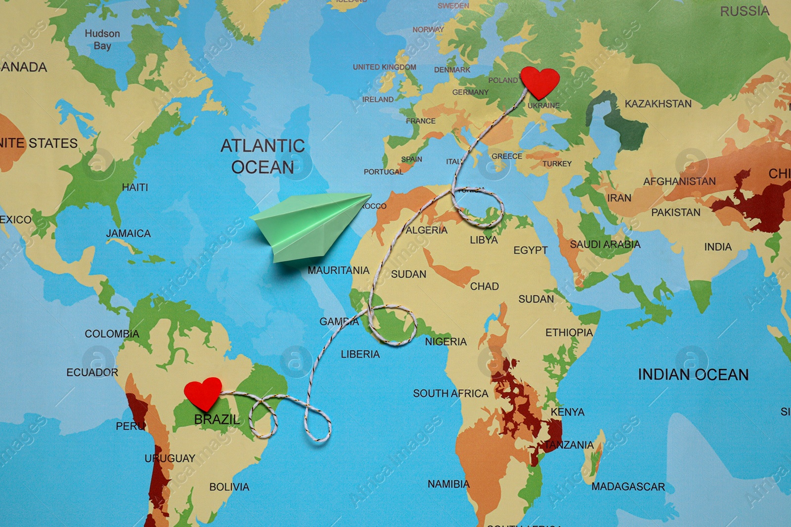 Photo of Paper plane and decorative cord between two red hearts on world map symbolizing connection in long-distance relationship, flat lay