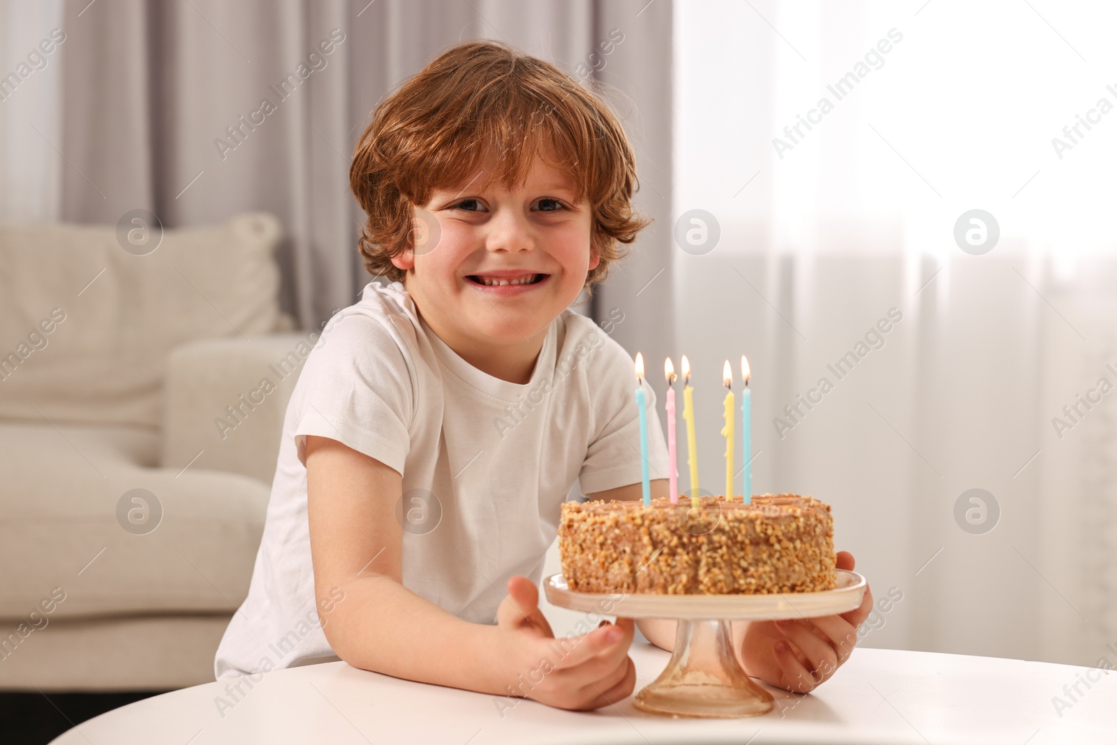 Photo of Cute boy with birthday cake at table indoors