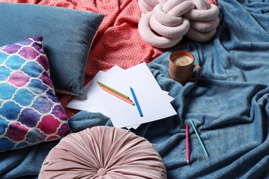 Photo of Composition with cup of coffee, pencils, pillows and plaid on bed