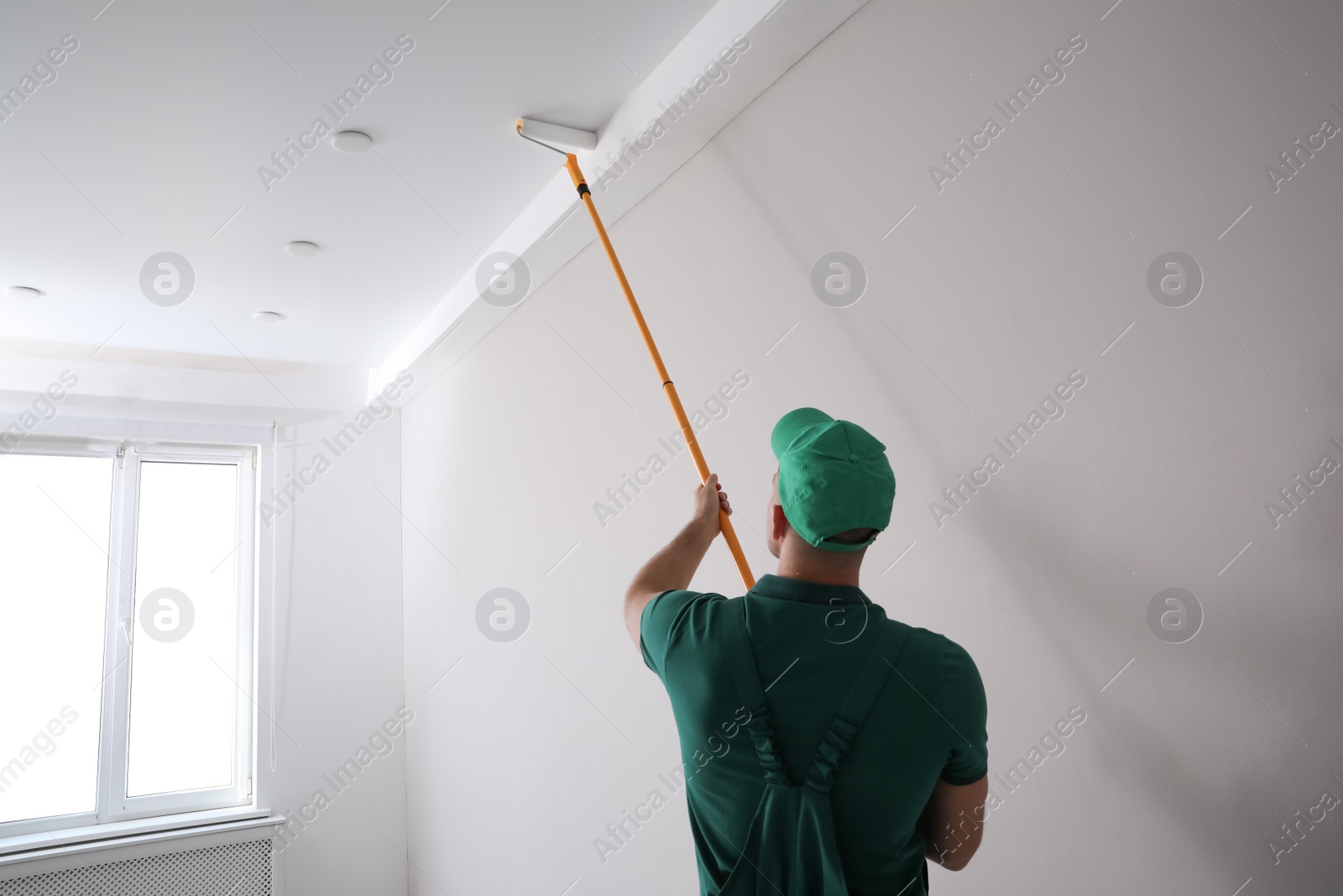 Photo of Man painting ceiling with roller in room, back view