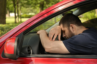 Tired man sleeping on steering wheel in his car