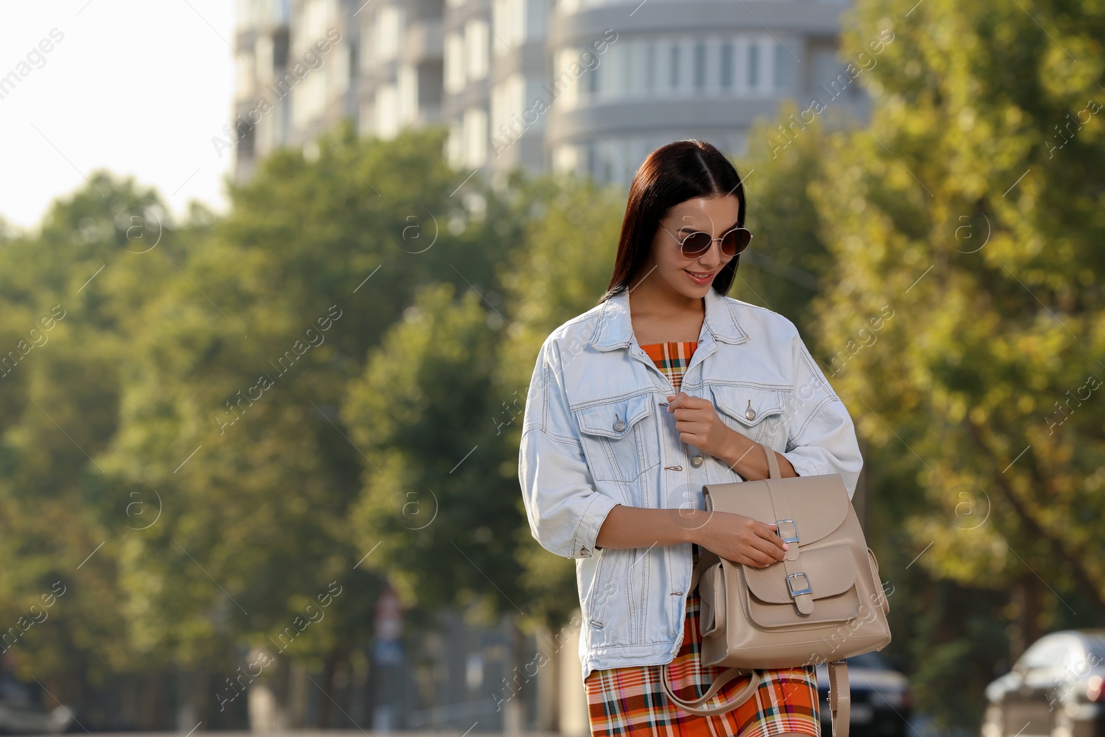 Photo of Beautiful young woman with stylish beige backpack on city street, space for text