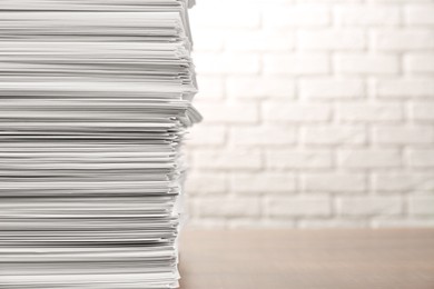 Stack of paper sheets on wooden table near white brick wall, space for text