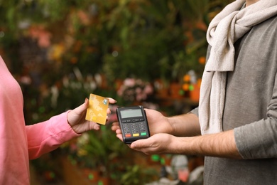 Photo of Woman using credit card for terminal payment in floral shop, closeup