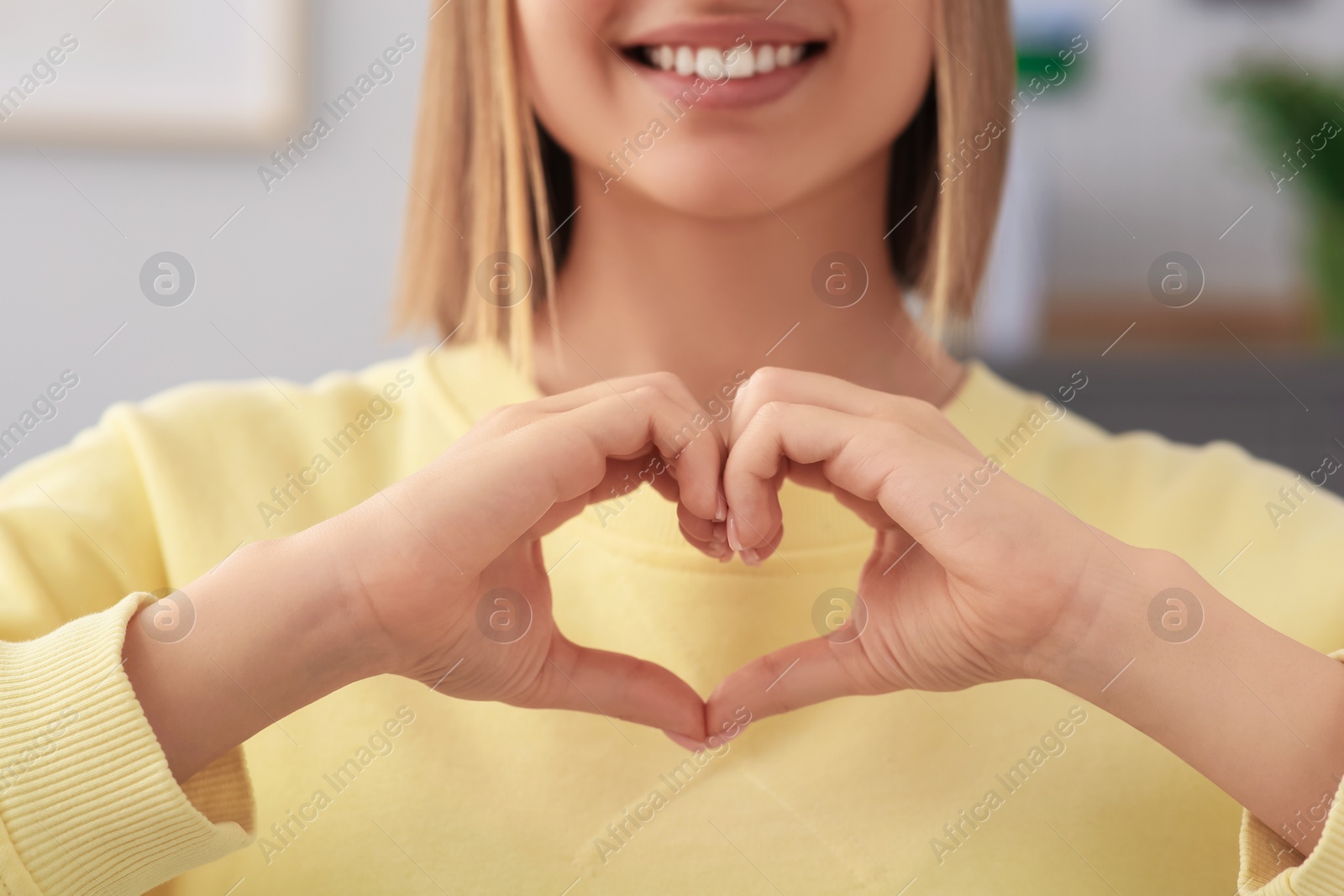 Photo of Young woman making heart with hands indoors, closeup. Volunteer concept