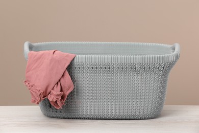 Photo of Plastic laundry basket with clothes near beige wall