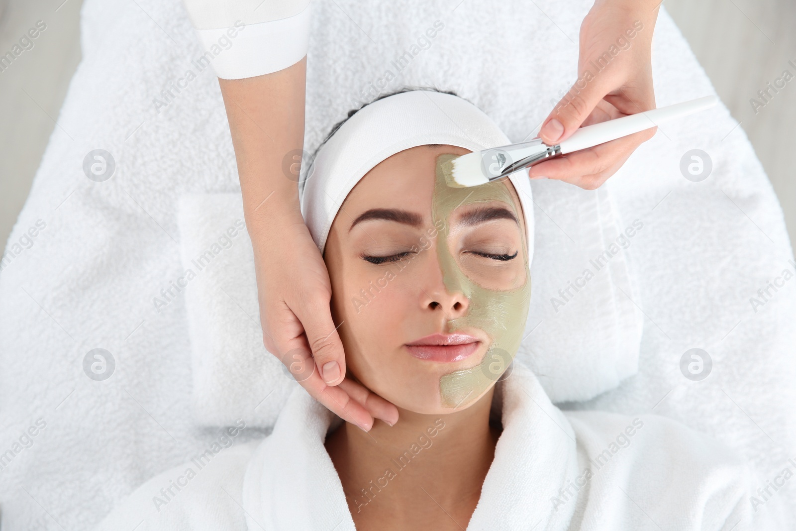 Photo of Cosmetologist applying mask on client's face in spa salon, above view