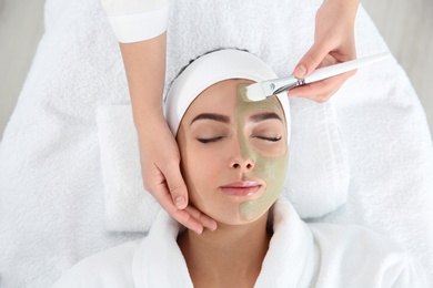 Cosmetologist applying mask on client's face in spa salon, above view