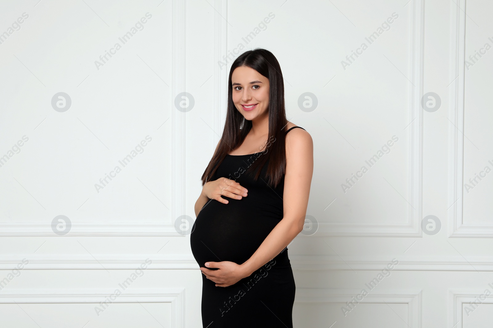 Photo of Beautiful pregnant woman in black dress near light grey wall