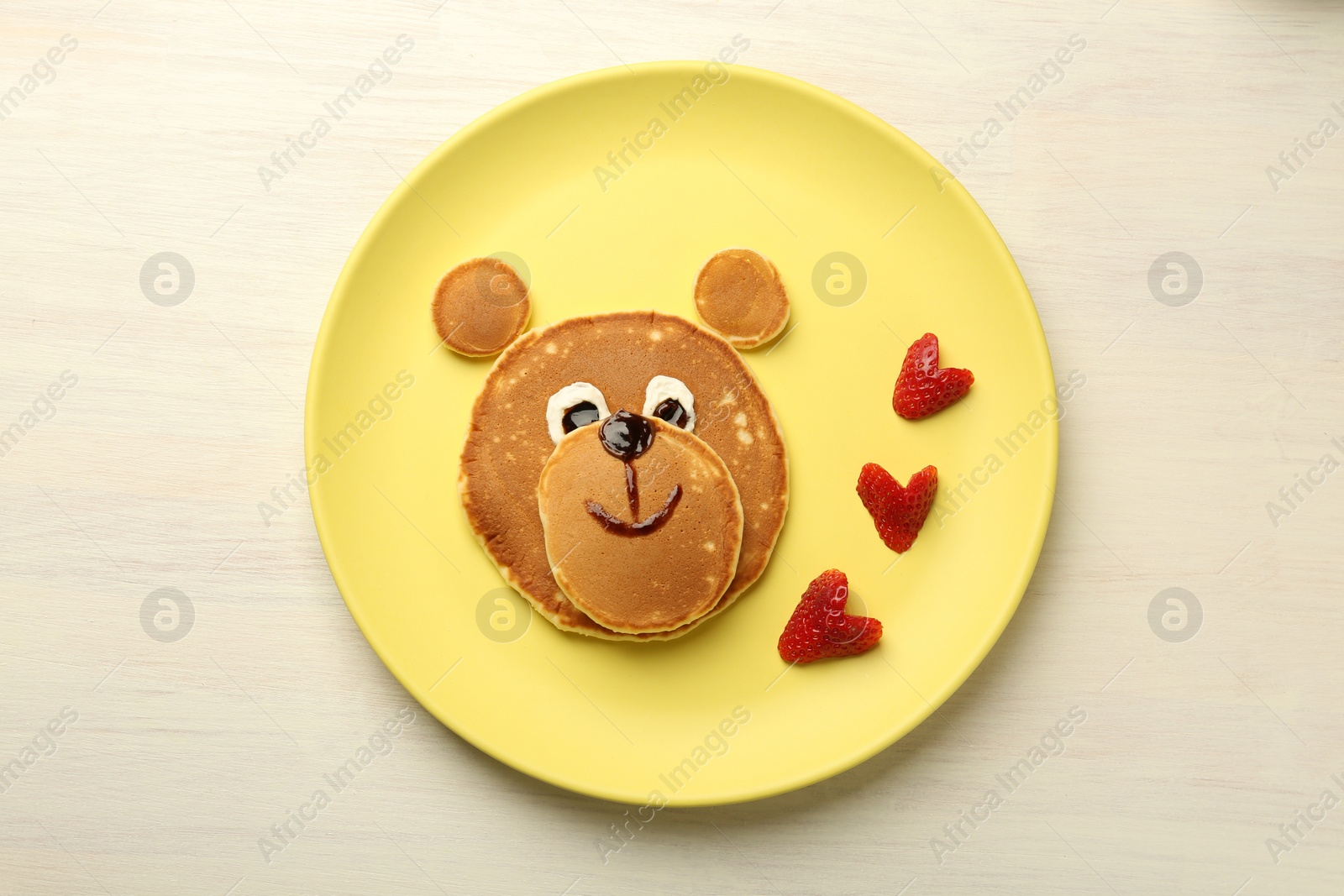 Photo of Creative serving for kids. Plate with strawberries, cute bear made of pancakes on light wooden table, top view