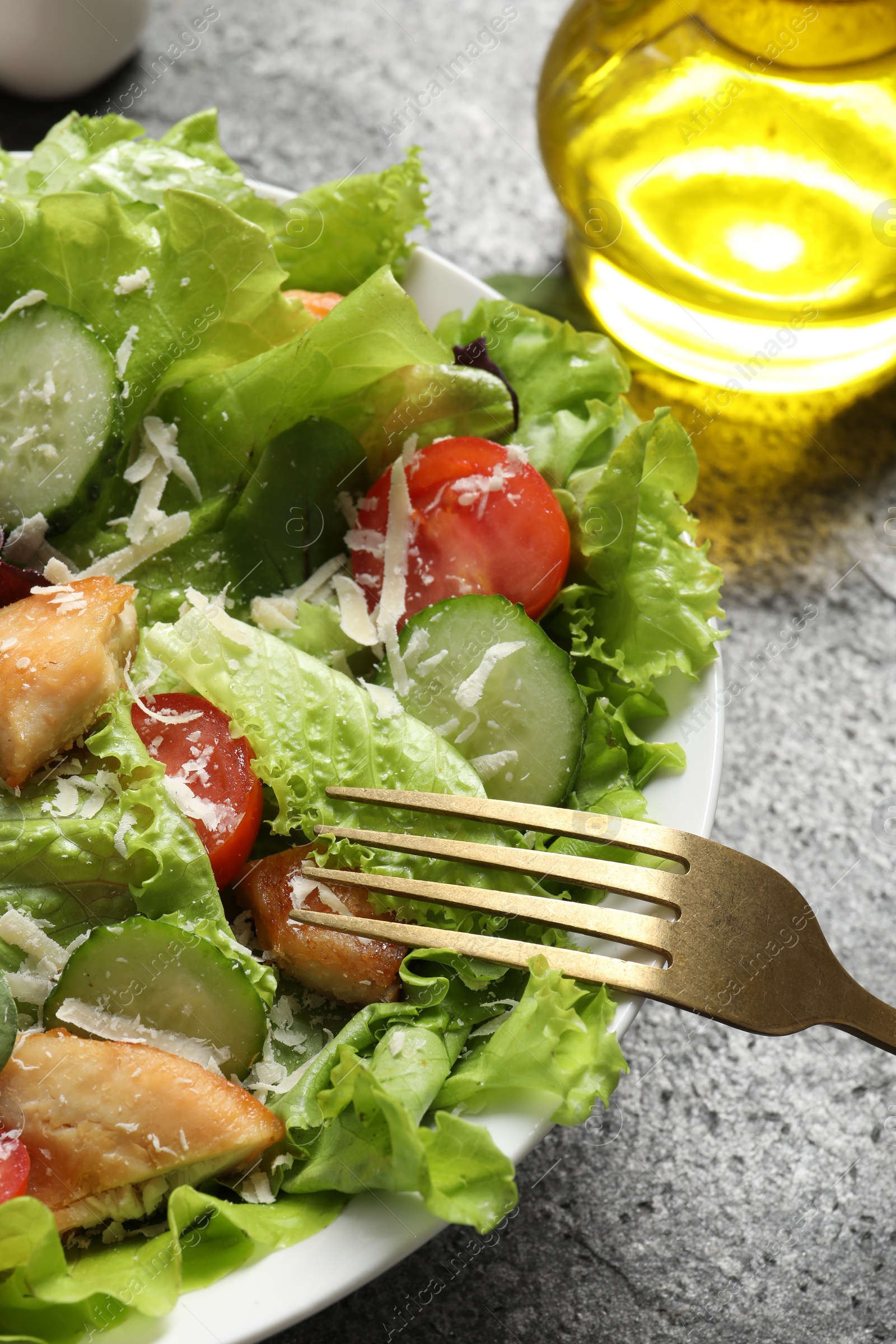 Photo of Eating delicious salad with chicken, cheese and vegetables at grey table, closeup